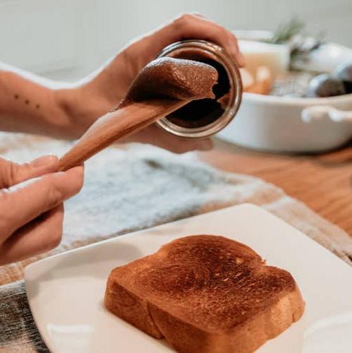 A jar of Cinnamon Creamed Honey with a golden, creamy consistency, surrounded by  fresh toast and a honey dipper.