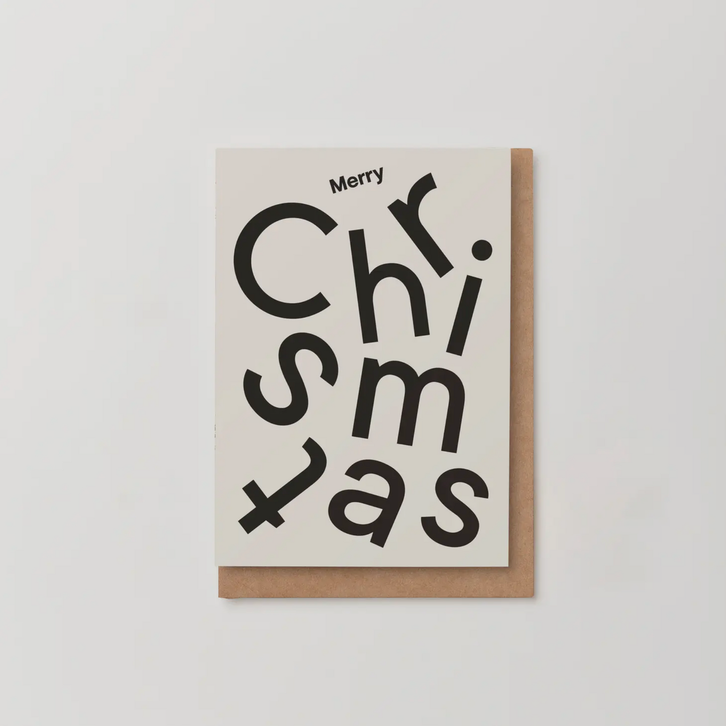 Minimalist Merry Christmas card with black type collage on off-white textured stock, paired with a premium GF Smith Kraft envelope.